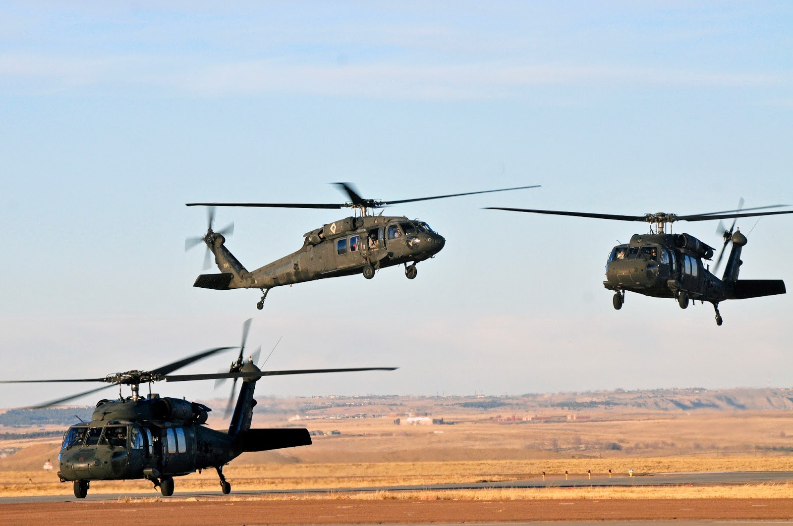 Three UH-60 Black Hawk helicopters maneuver during training over open terrain
